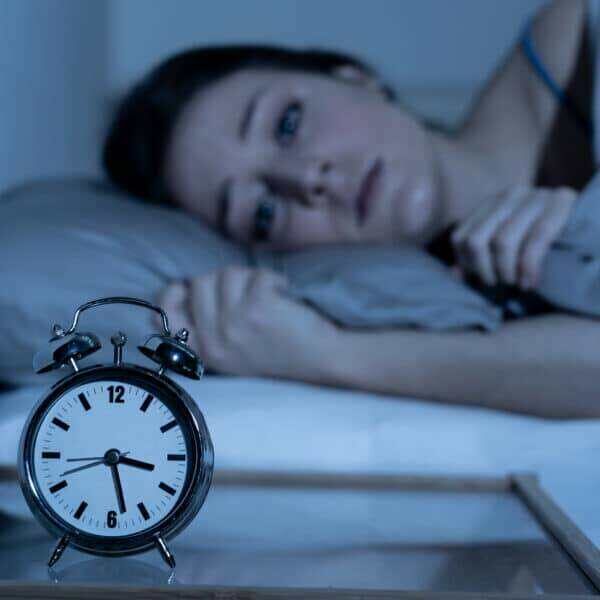 Sleepless and desperate beautiful caucasian woman awake at night not able to sleep, feeling frustrated and worried looking at clock suffering from insomnia in sleep disorder concept.